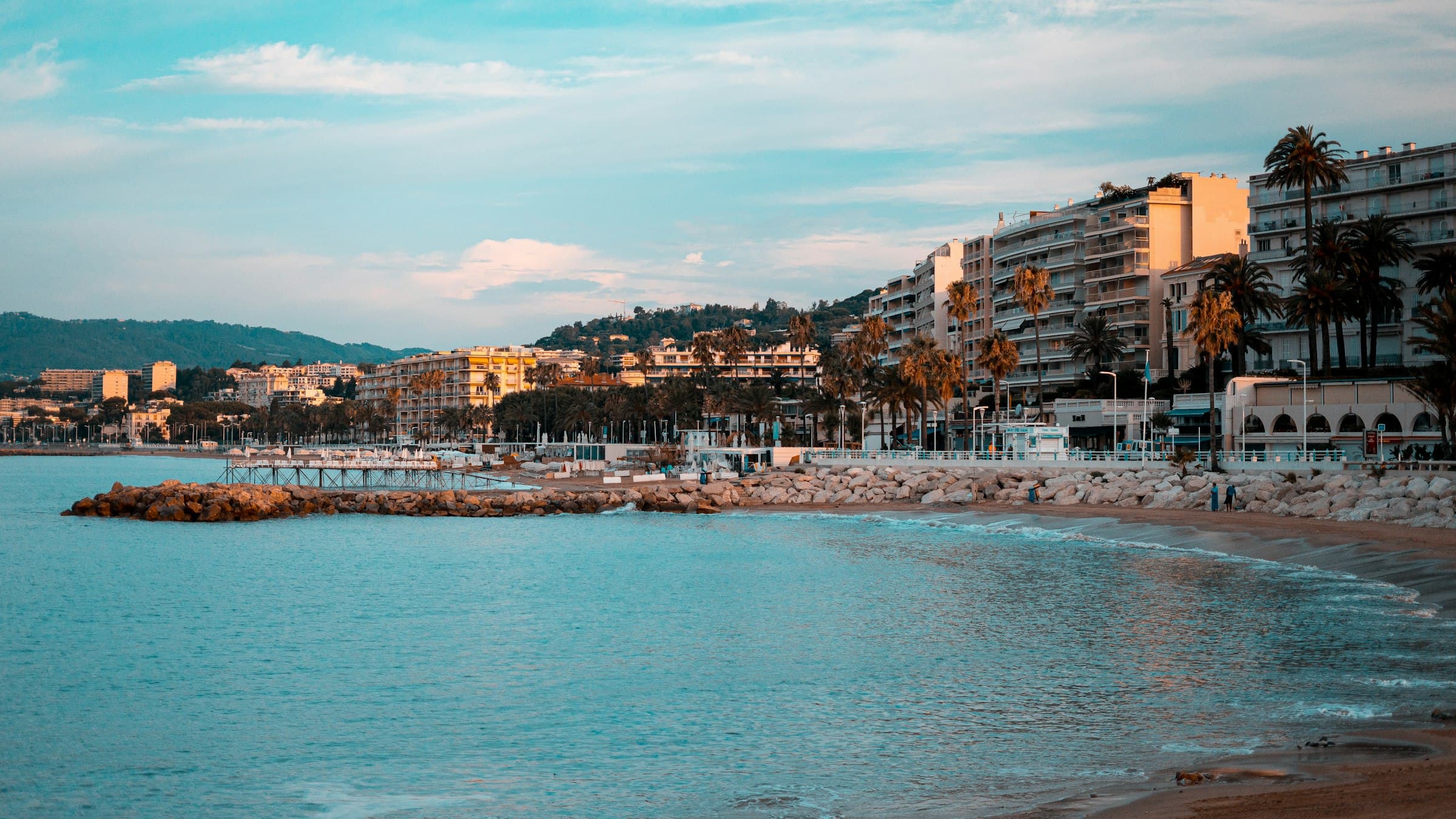 The Croisette curving along the Bay of Cannes at golden hour, the grand hotels facing the water.