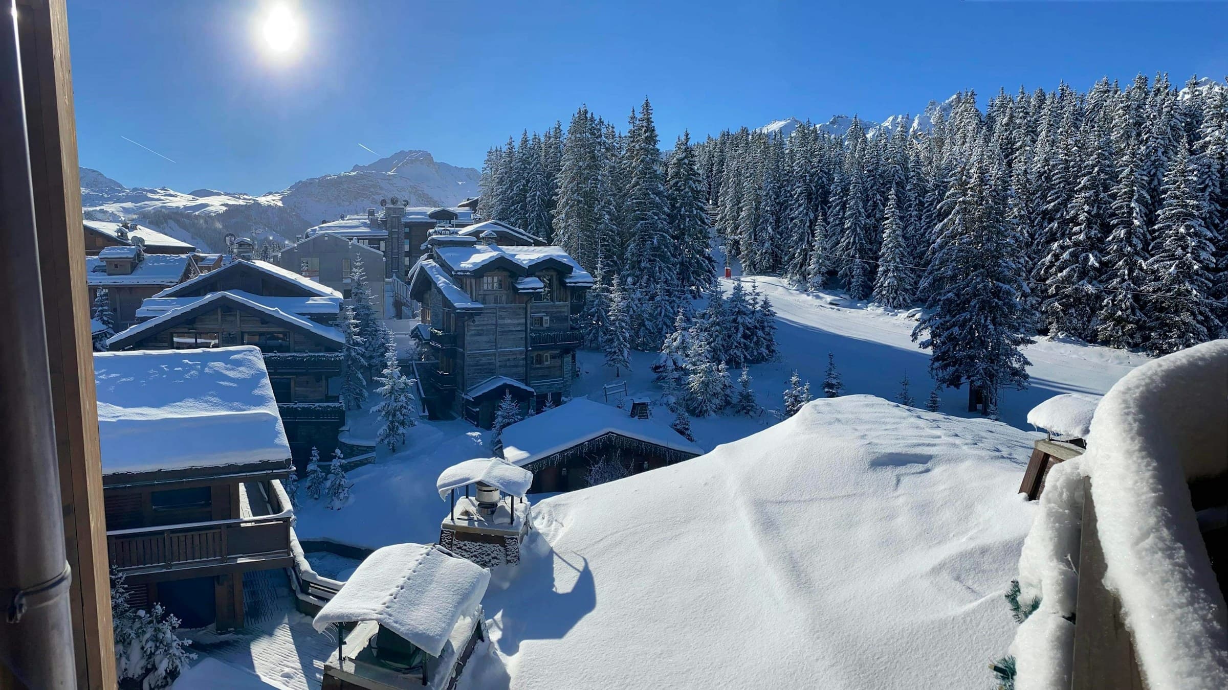Snow-laden Courchevel rooftops and pine slopes seen from a chalet window on a bluebird morning.