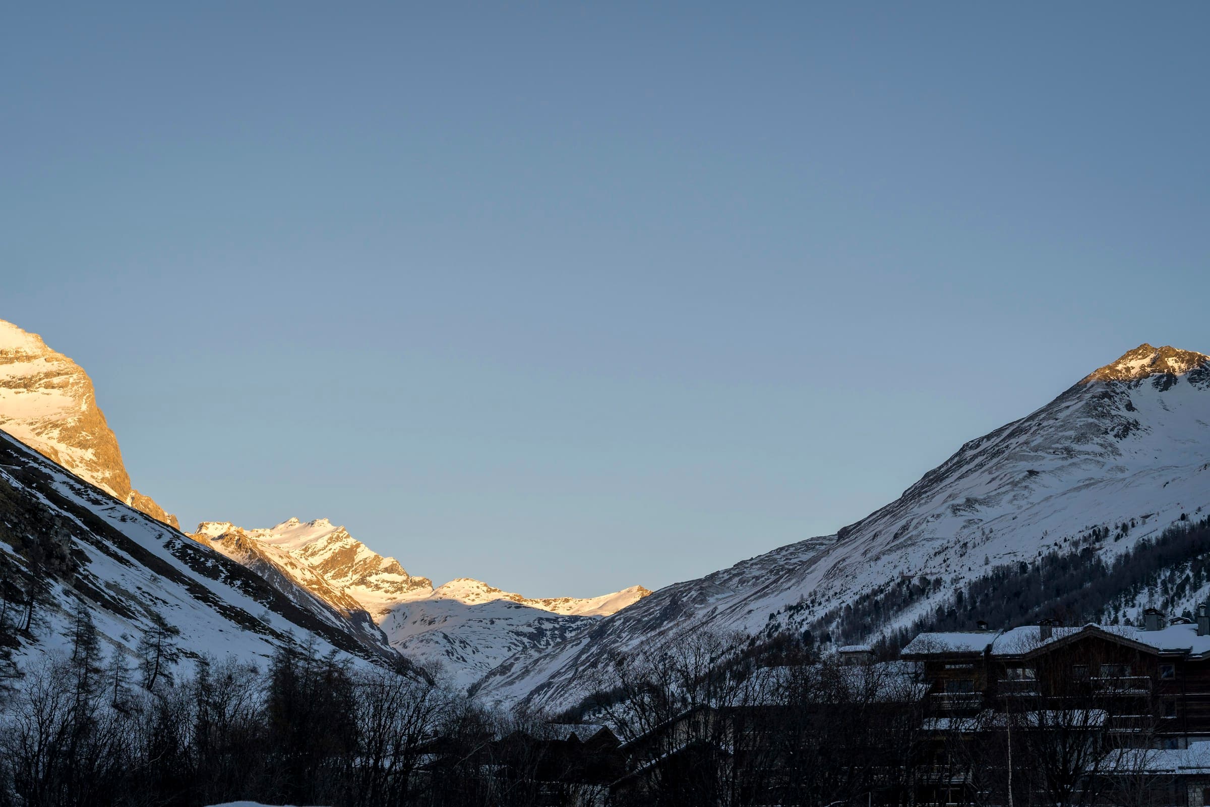 Snow peaks above Val d'Isère lit by alpine first light, the village still in valley shadow.