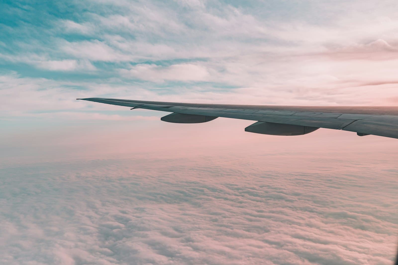 An aircraft wing against a sunset sky, soft golden cloud cover below.
