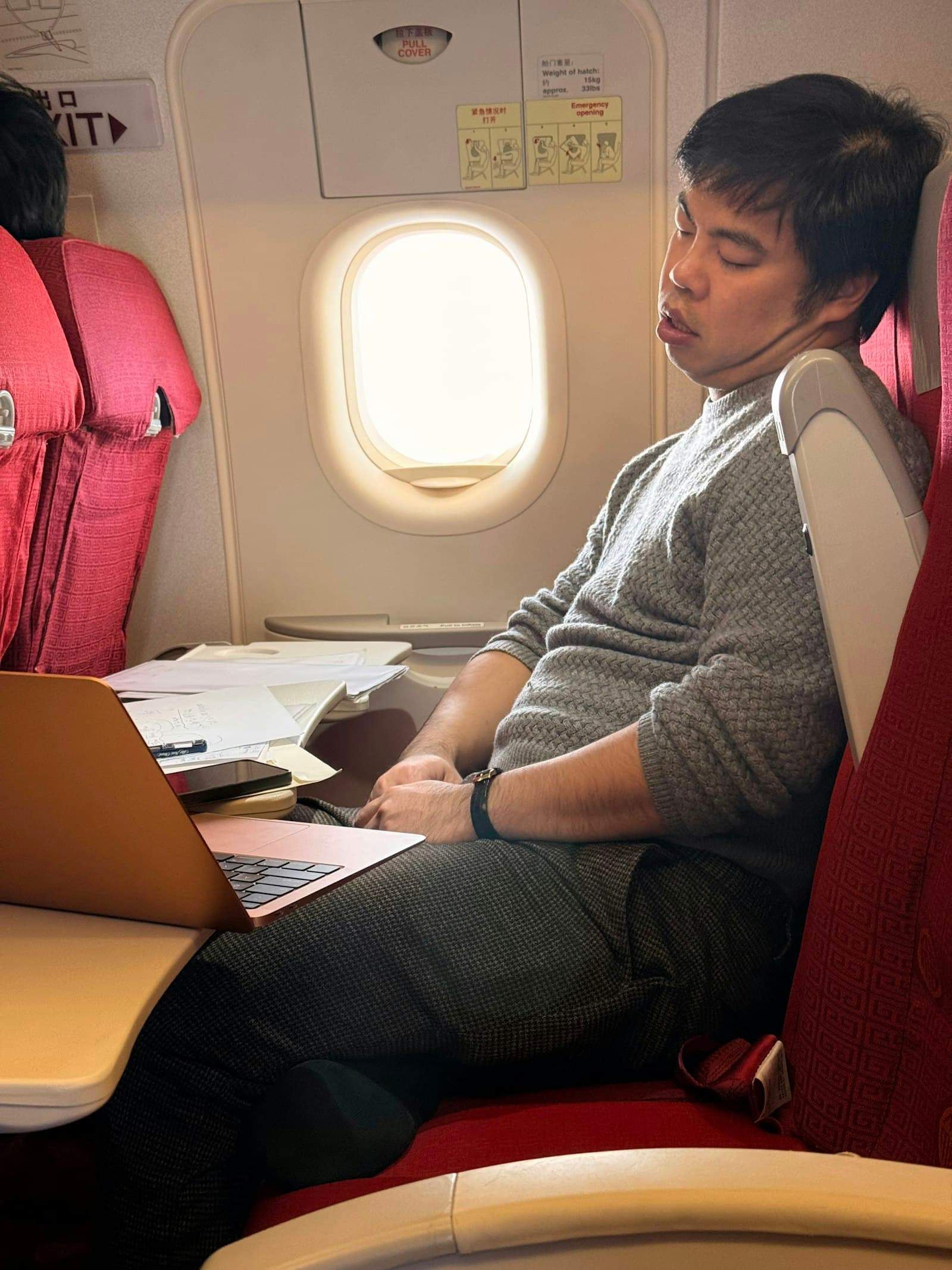An open laptop on a cabin tray-table, daylight from a window.