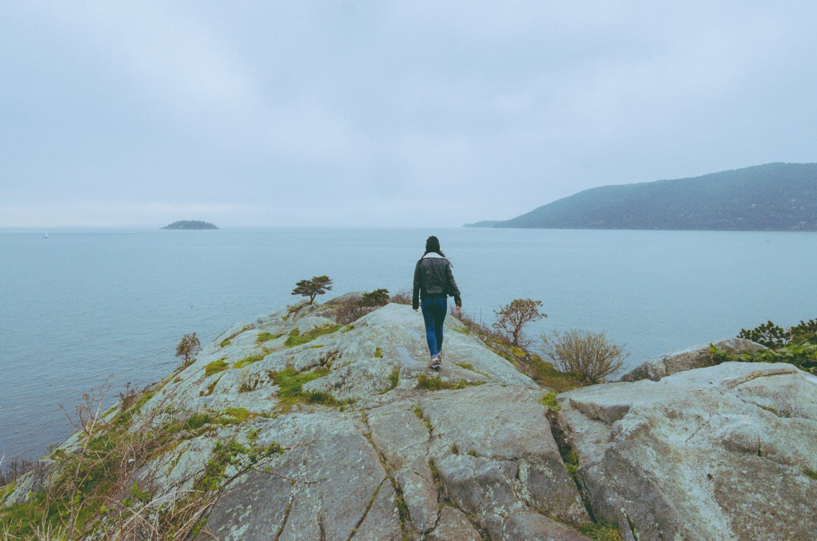 A figure walking alone along a coastal cliff path.